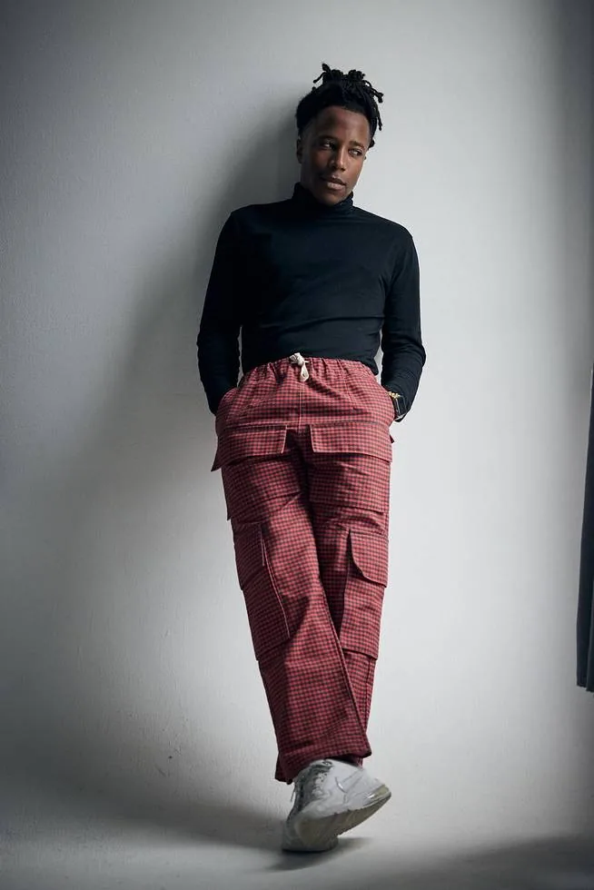 Chad Chambers in a black turtleneck and red patterned pants leaning against a wall