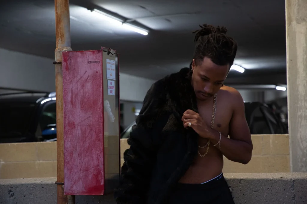 Chad Chambers posing in a parking garage with a black fur coat and gold chains